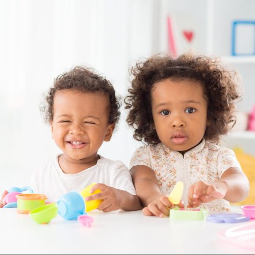Portrait of a little girl posing at camera while her brother laughing and playing in the nursery